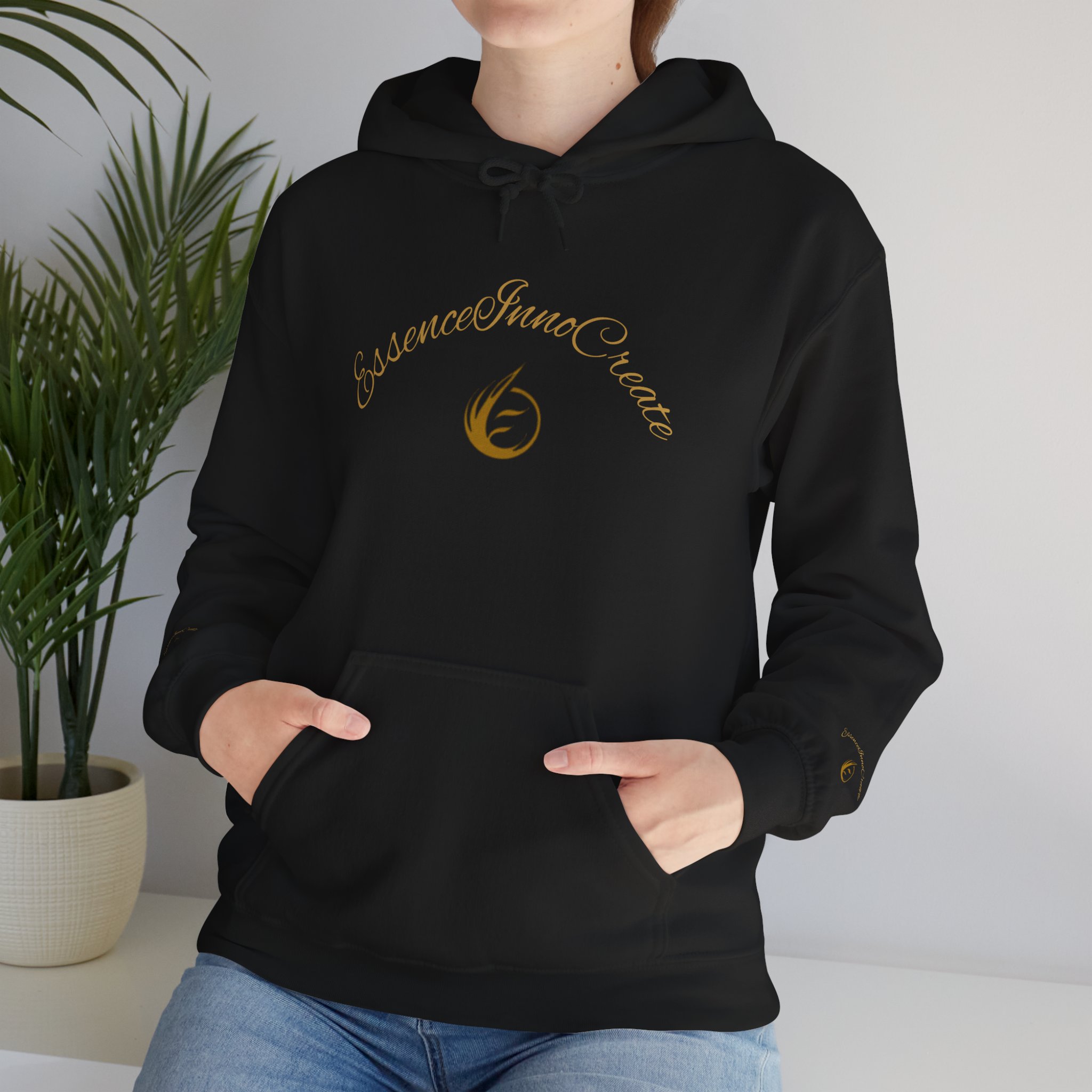 10048503102287861057_2048jpeg - Essence Innovation Person wearing a black hoodie with a gold cursive logo on the chest, seated near a potted plant.