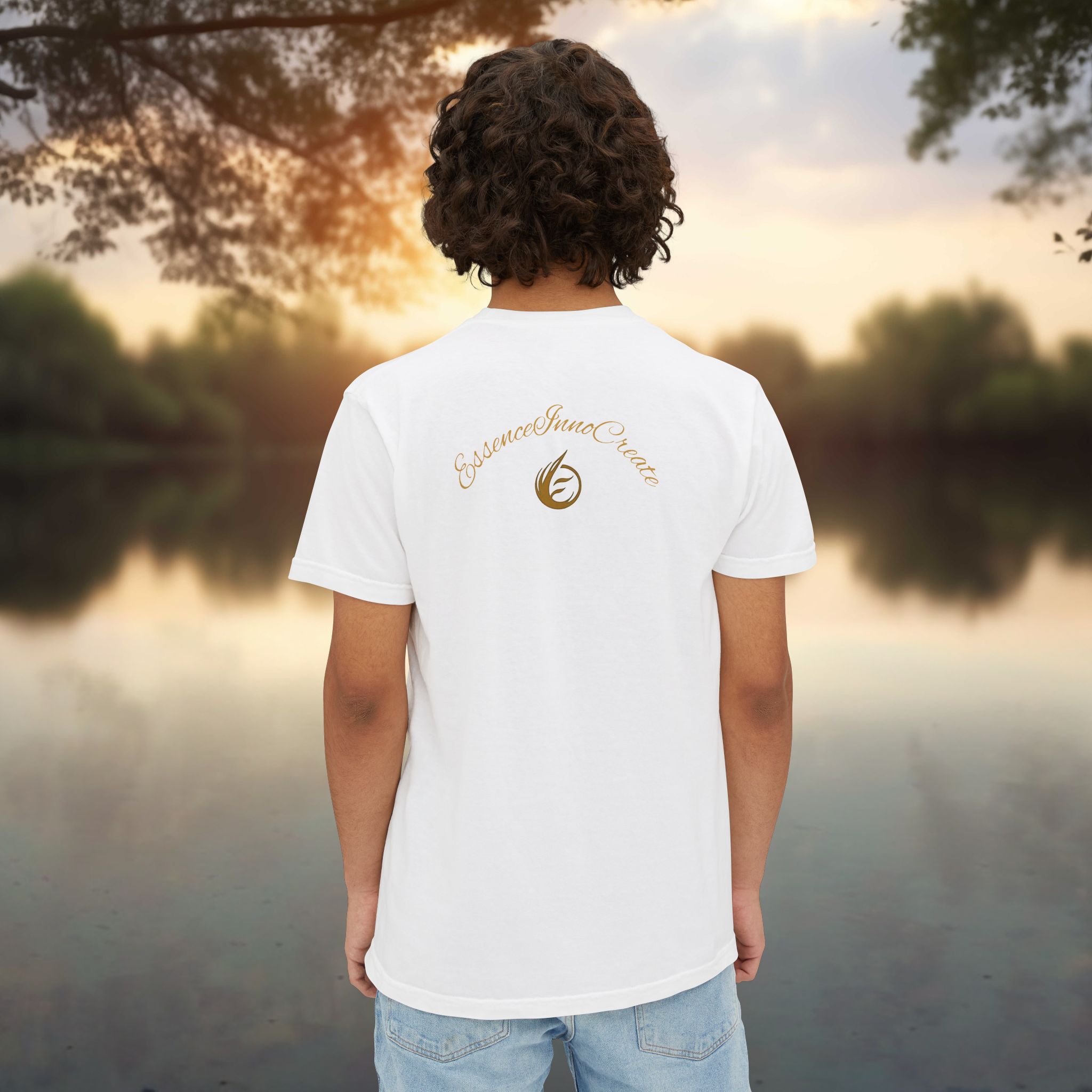 10513134715596730573_2048_customjpeg - Essence Innovation Person standing with back to camera, wearing a white T-shirt with a gold emblem on the back, outdoors at sunset by a body of water