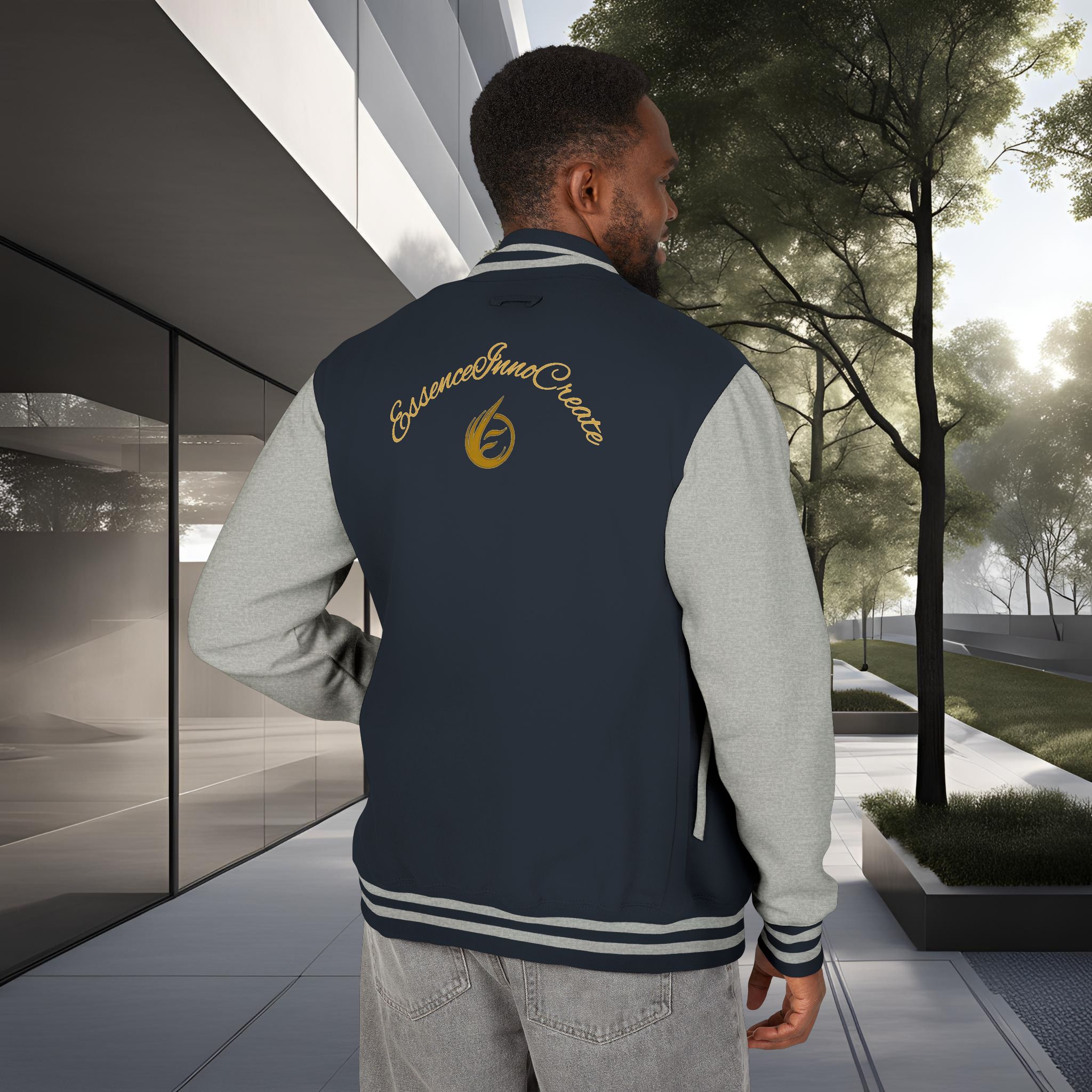 11496501184026293651_2048_customjpeg - Essence Innovation Back view of a person wearing a navy jacket with grey sleeves and gold cursive embroidery, standing in a modern outdoor setting with glass building on the left and trees on the right.
