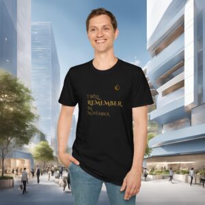 Man in a black T-shirt stands in a modern urban plaza with glass buildings and a crowd in the background, smiling at the camera.