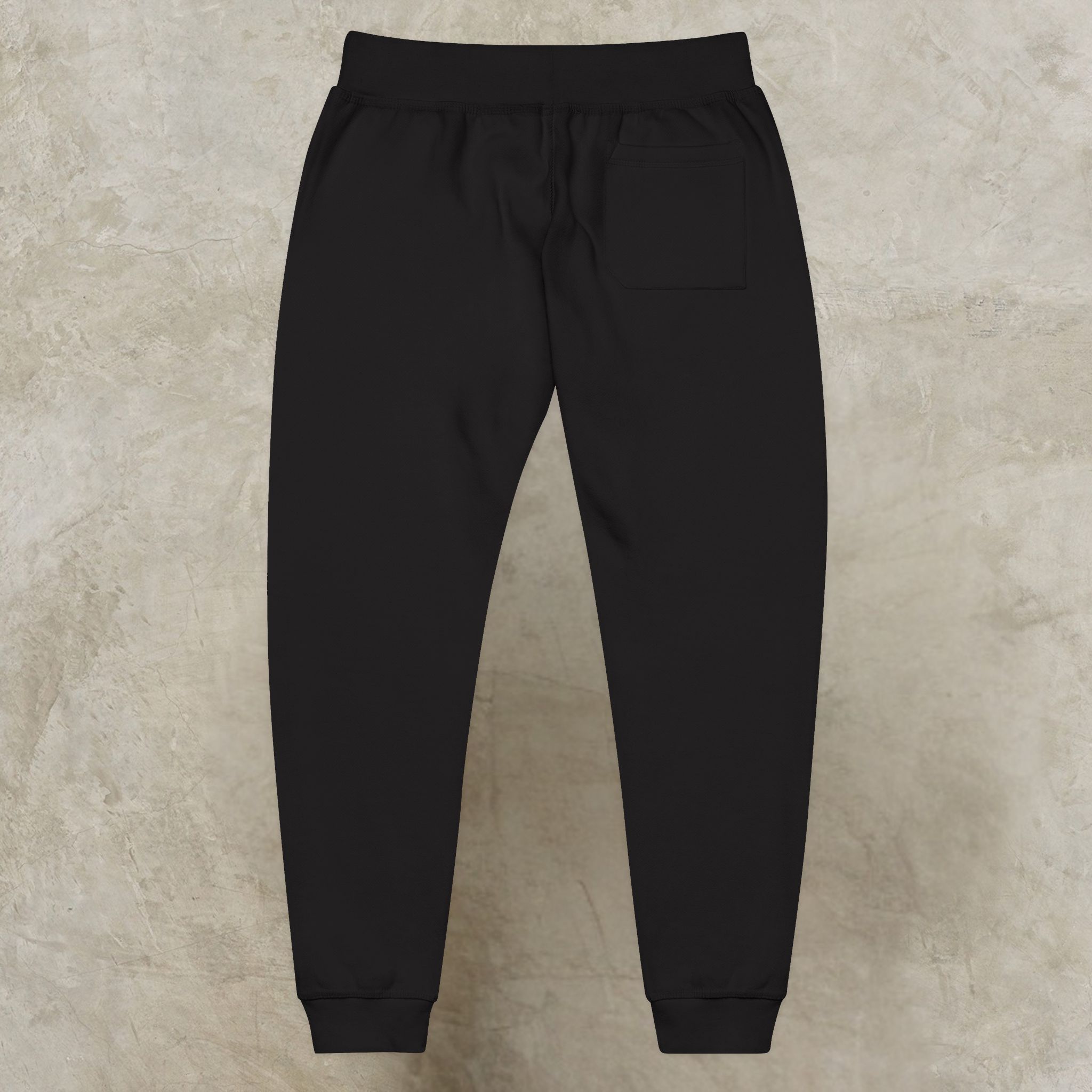1380221284911121501_2048_customjpeg - Essence Innovation Back view of black jogger pants with elastic waistband and single rear pocket against a textured floor background.