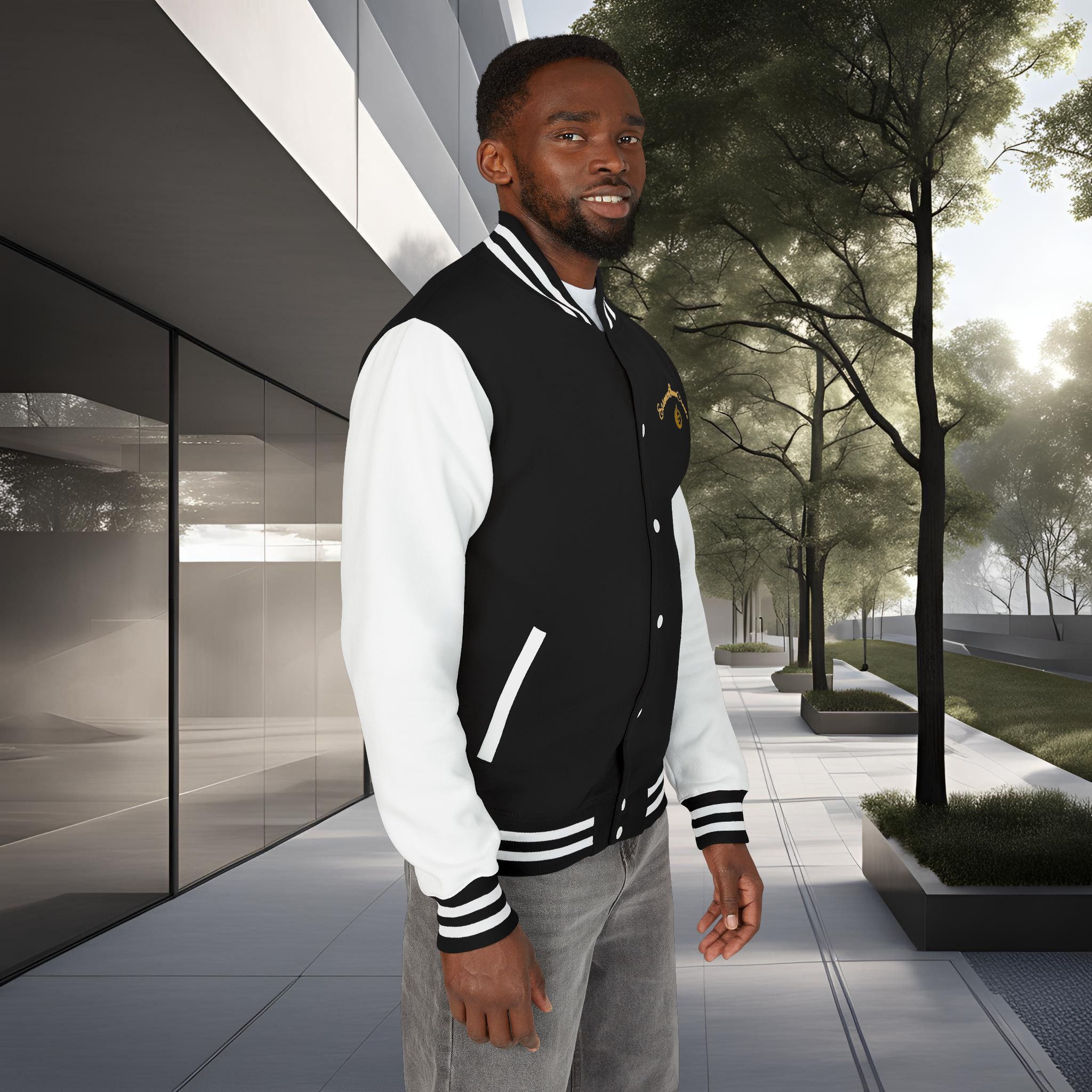 14877942888733909051_2048_customjpeg - Essence Innovation Man wearing a black and white varsity jacket stands near a modern glass building with trees in the background.