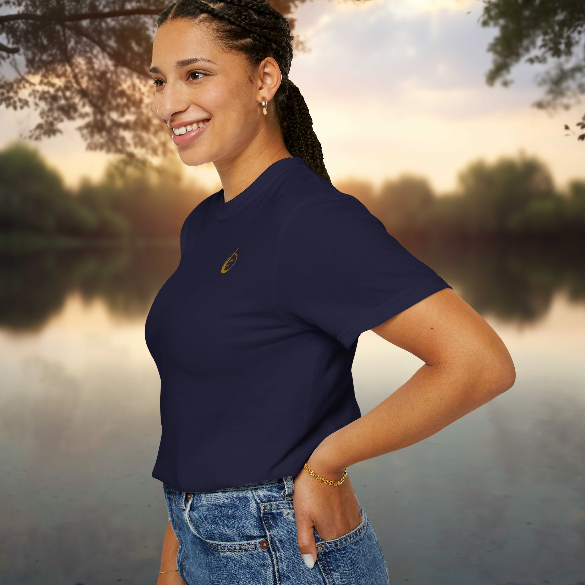 16453324043375795785_2048_customjpeg - Essence Innovation Person with braided hair wearing a navy shirt and denim shorts standing by a lake at sunset, smiling in profile view.