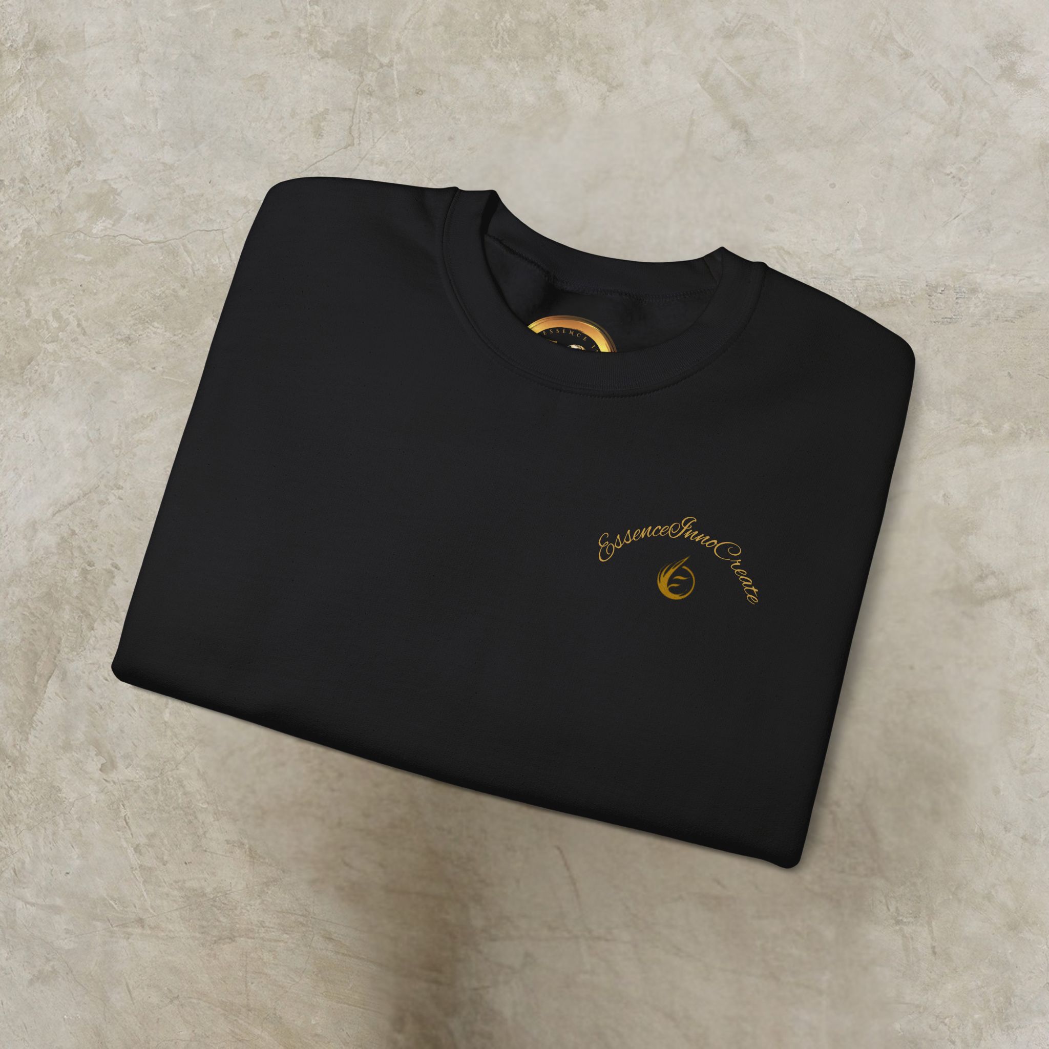 16731959766474830516_2048_customjpeg - Essence Innovation Black folded t-shirt on a light background, gold circular logo visible near the neckline and a gold-tag peeking from the collar.