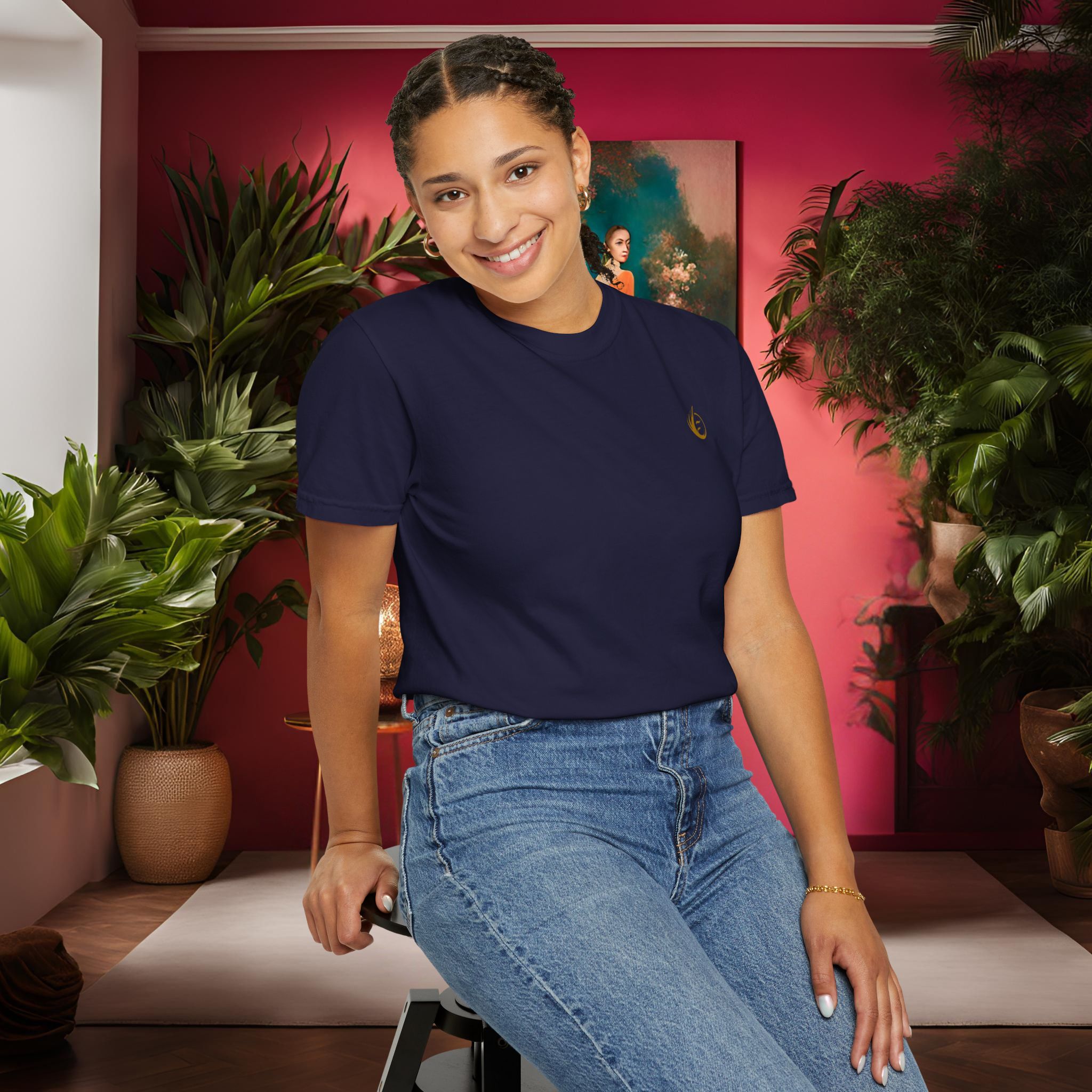 1687698303336762749_2048_customjpeg - Essence Innovation Smiling woman in a navy top and jeans sits on a stool in a pink-walled room with green plants behind her.
