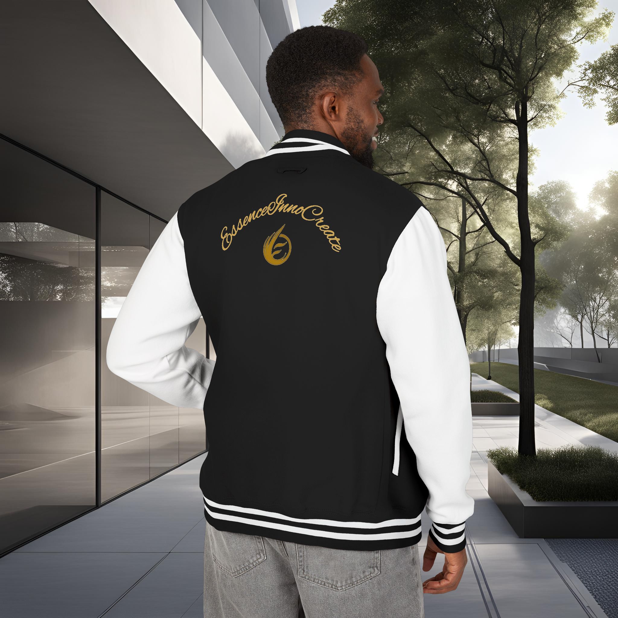 4904354586387019024_2048_customjpeg - Essence Innovation Back view of a man wearing a black and white varsity jacket with gold script on the back, standing outside near a modern glass building and trees.
