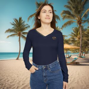 5500424036883409613_2048_custom-2jpeg - Essence Innovation Woman standing on a sandy beach with palm trees, wearing a navy long-sleeve top and blue jeans.
