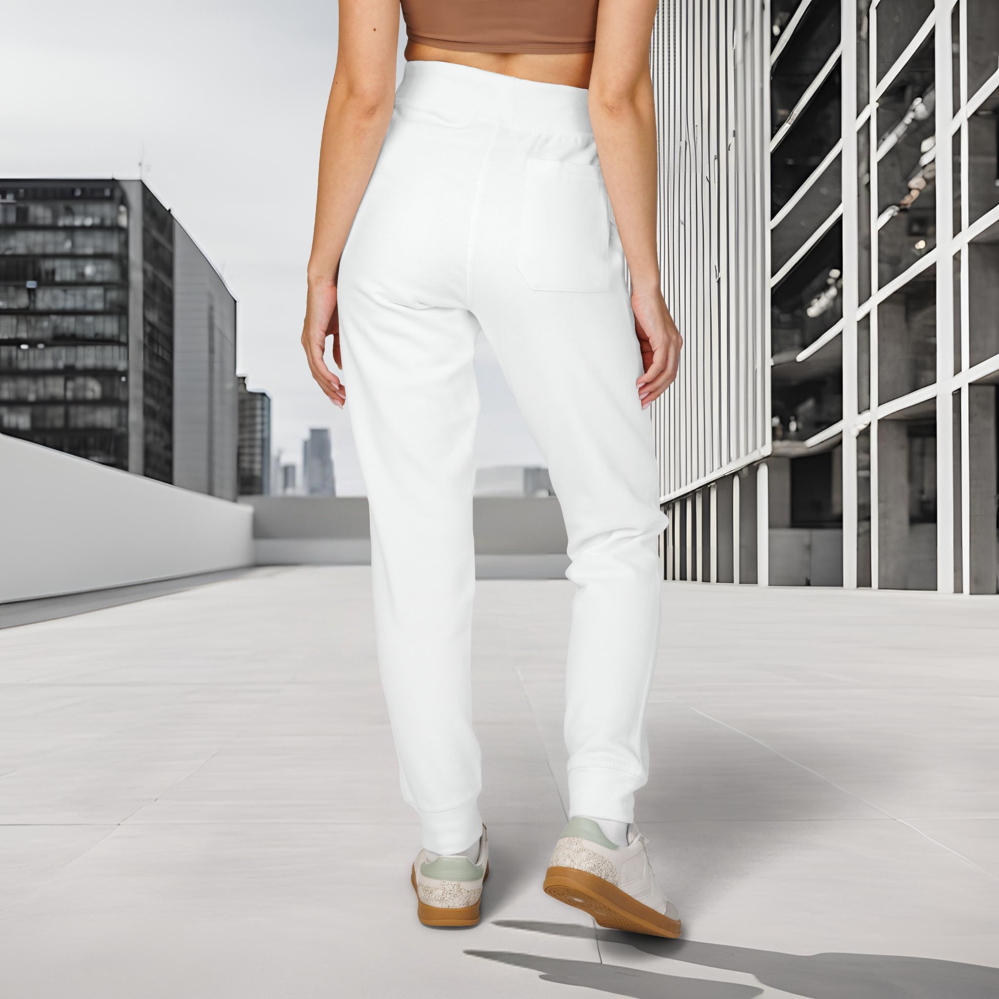 5809903782953502637_2048_customjpeg - Essence Innovation Back view of a person wearing white pants and light sneakers, walking on a white tiled rooftop with modern glass buildings in the background.