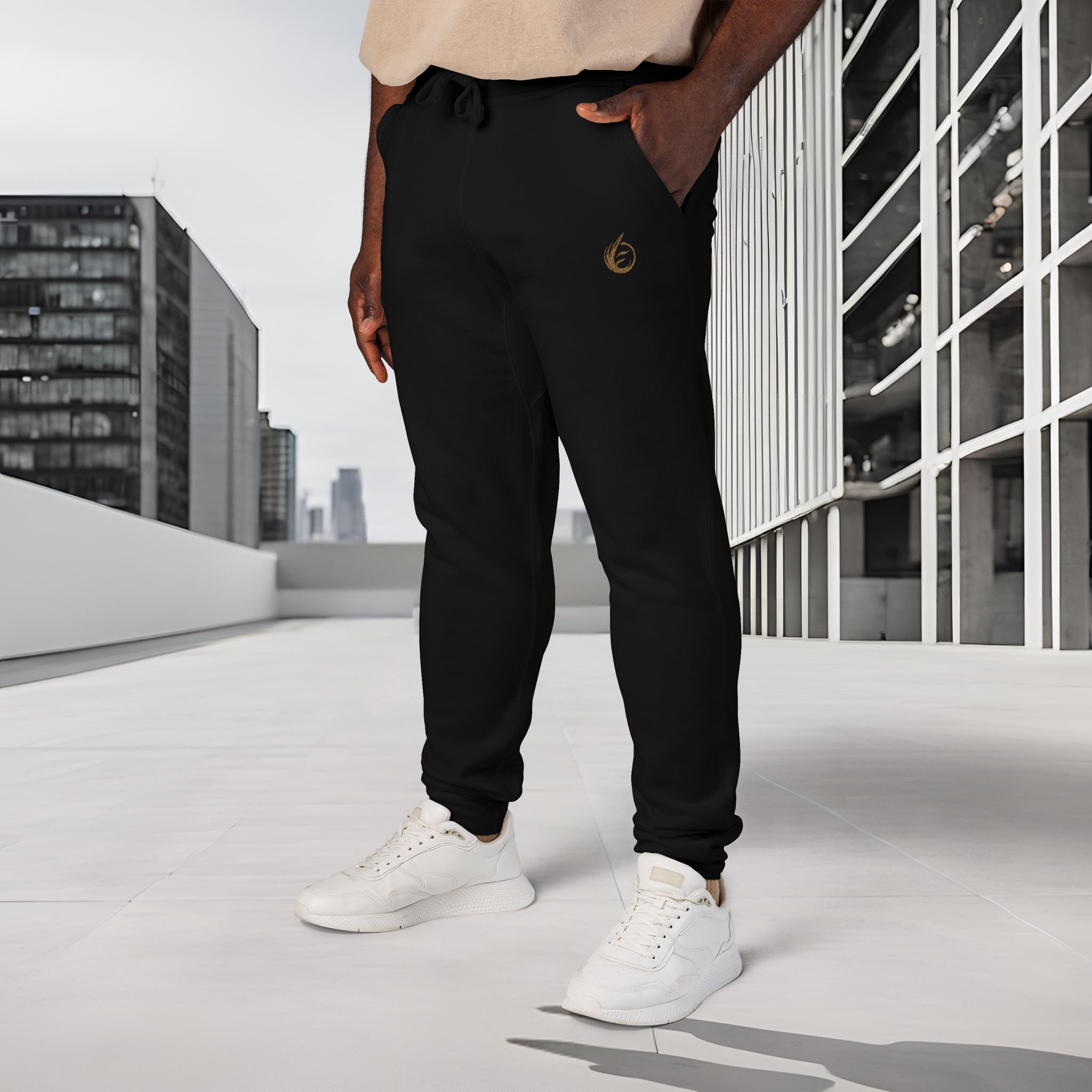 646651728501294307_2048_customjpeg - Essence Innovation Close-up of a person wearing black jogger pants with a small gold logo, beige top, and white sneakers on a rooftop with city buildings in the background.