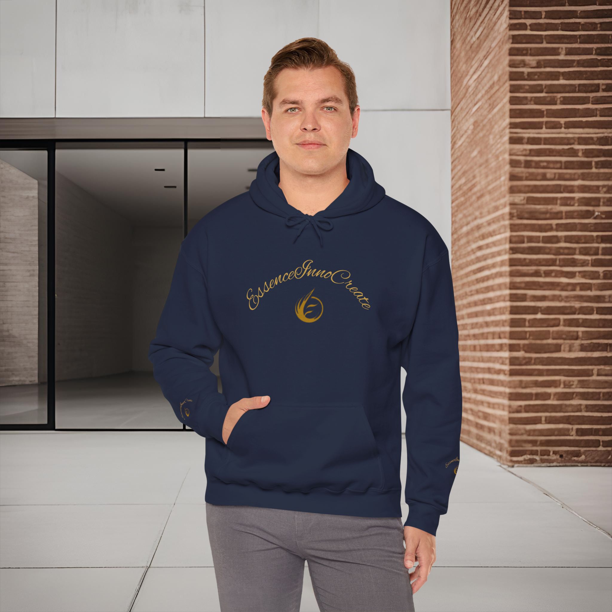 752806163410404573_2048_customjpeg - Essence Innovation Man wearing a navy hoodie with gold script logo standing in a modern interior with white cabinets and brick wall on the right; hands in pockets.
