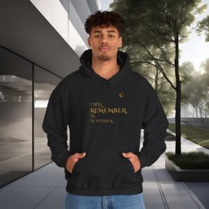 Young man in a black hoodie with gold text reading 'I WILL REMEMBER IN NOVEMBER' standing outdoors near a modern glass building.