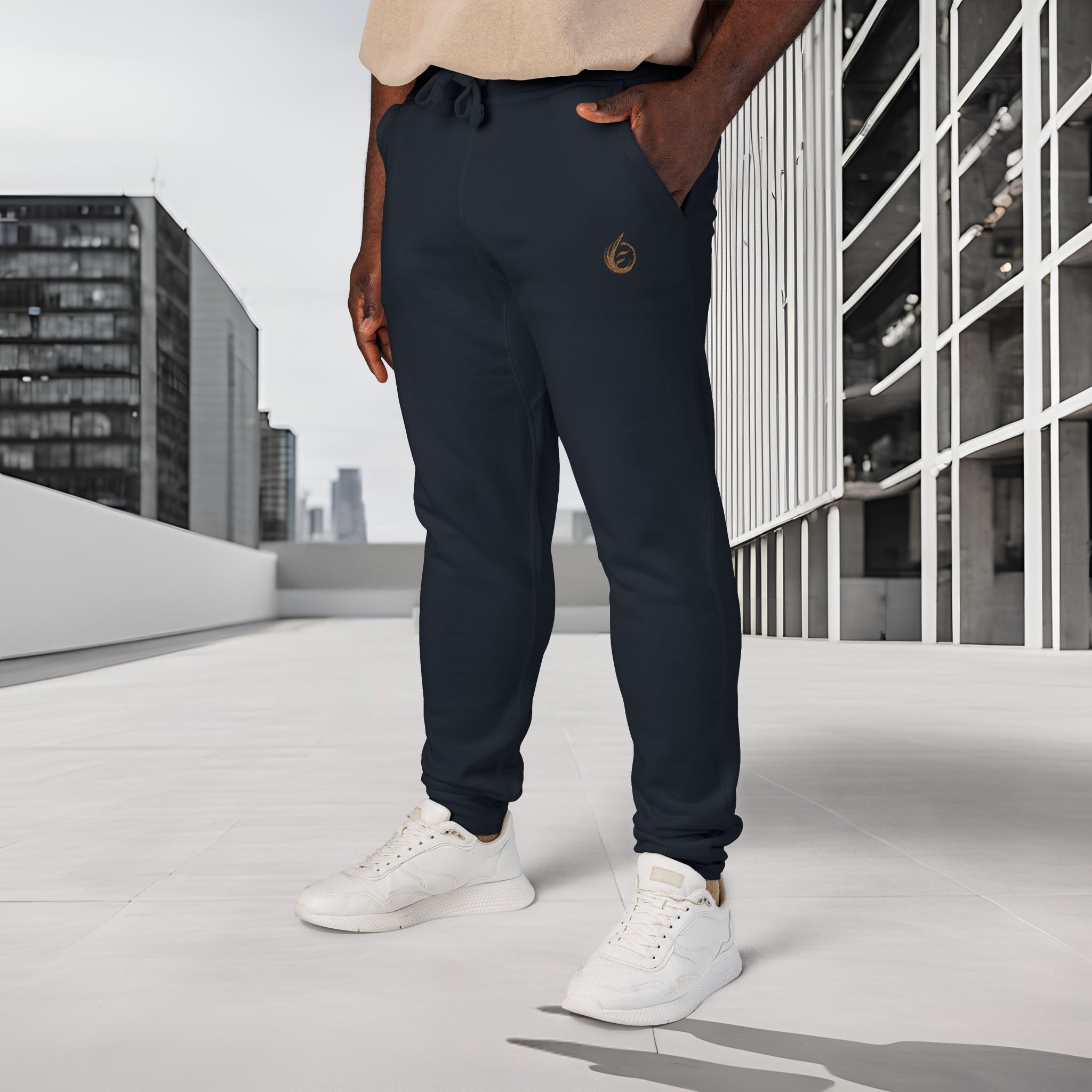 9112208065296907226_2048_customjpeg - Essence Innovation Person standing outdoors wearing navy jogger pants with a gold emblem and white sneakers on a modern rooftop.