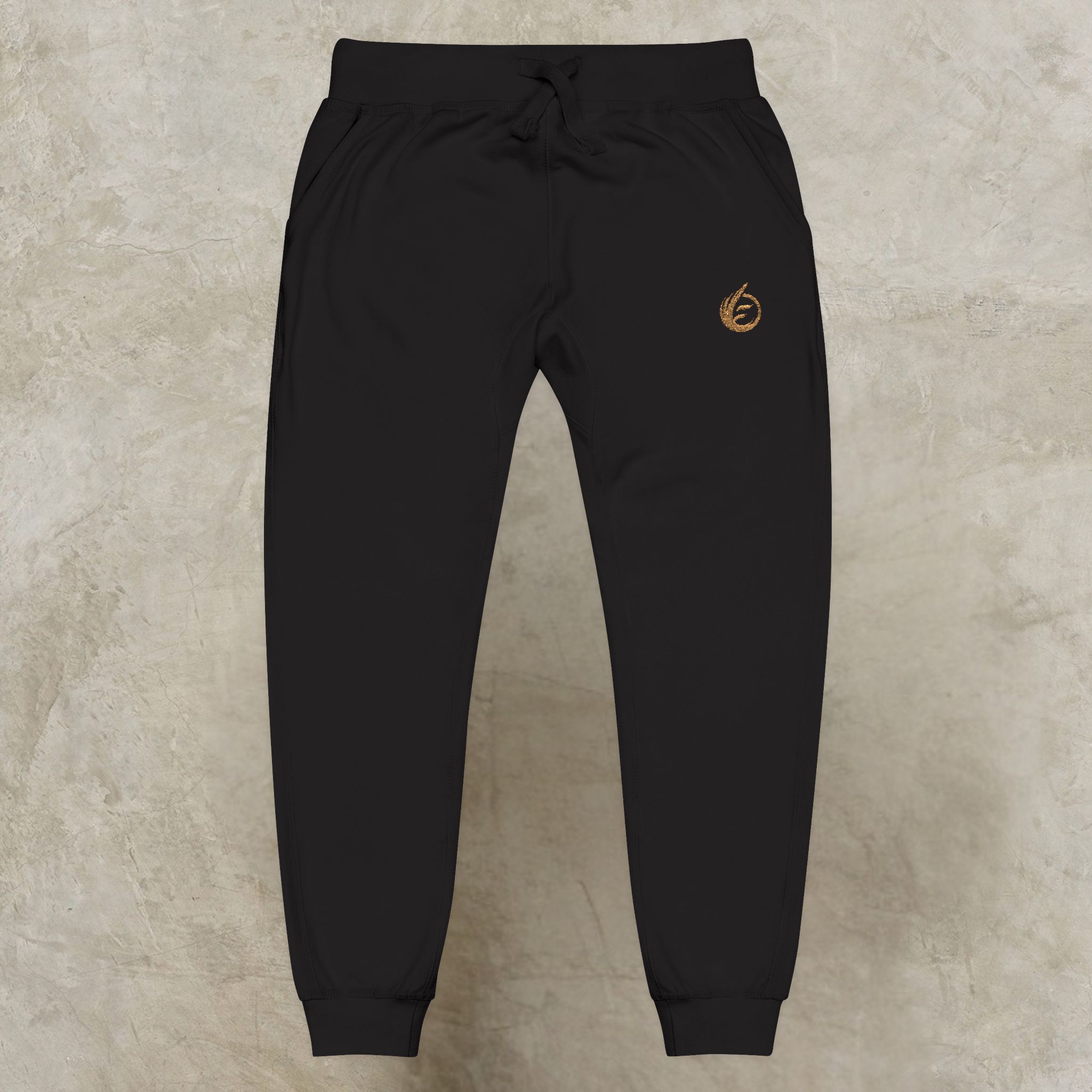 998964579342324387_2048_customjpeg - Essence Innovation Black athletic joggers with a small gold embroidered logo on the right thigh and a drawstring waistband, tapered cuffs visible at the ankles.